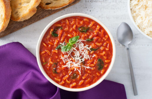 White bowl with tomato rice soup topped with cheese, and toasted bread