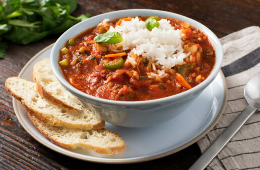 White bowl filled with tomato soup with rice and basil topped with cheese